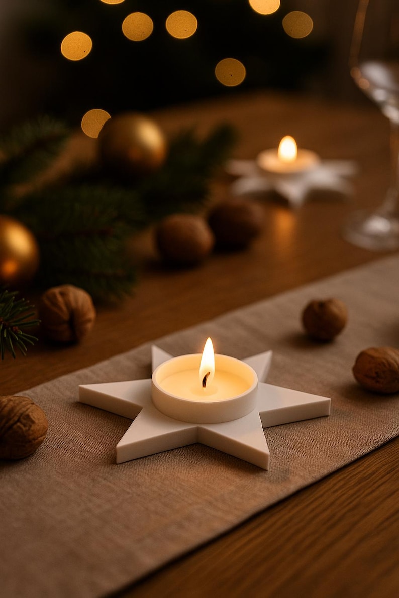 May include: A lit candle in a white star-shaped holder sits on a tan table runner. Walnuts and gold ornaments are scattered around the candle. The background is blurred with bokeh lights and greenery, creating a warm, festive atmosphere.