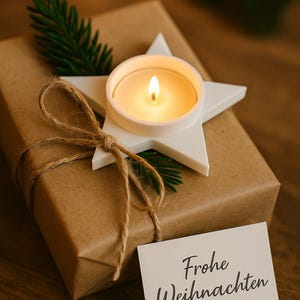 May include: A wrapped gift box with a white star-shaped candle holder and a lit candle. The box is wrapped in brown paper and tied with twine. A small card with the words "Frohe Weihnachten" is attached.