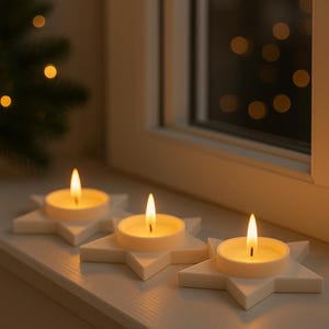 May include: Three lit tea light candles in star-shaped holders. The candles are white and the holders are a light cream color. The flames are bright yellow. The candles are placed on a white windowsill near a window.