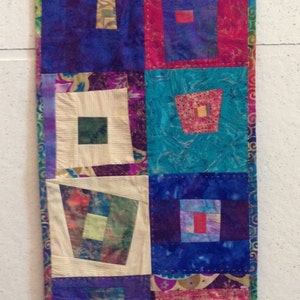 May include: A colorful patchwork quilt with a variety of fabrics and patterns. The quilt is made up of squares and rectangles, and it features a variety of colors, including red, blue, green, and purple. The quilt is edged with a gold trim. The quilt is labeled "Silk Quilt".