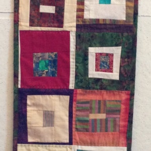 Puede incluir: Una larga pared rectangular hecha de cuadrados de tela en varios colores y patrones. Los cuadrados est&aacute;n cosidos juntos para crear un dise&ntilde;o de patchwork. La pared tiene un borde verde, rojo y blanco.