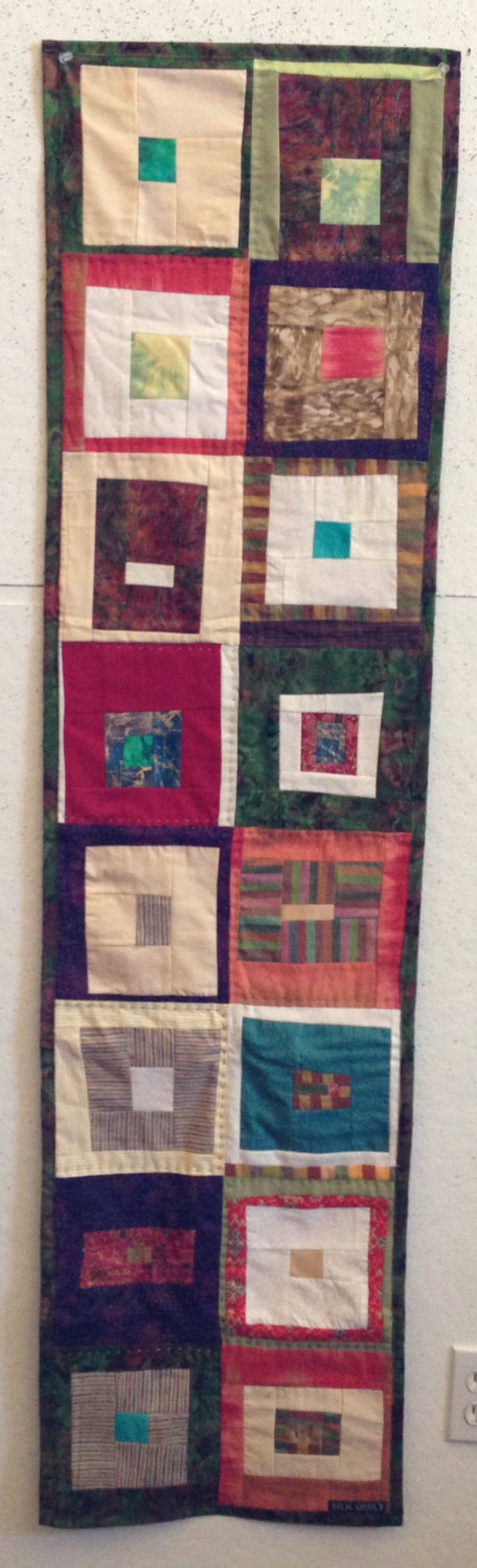Puede incluir: Una larga pared rectangular hecha de cuadrados de tela en varios colores y patrones. Los cuadrados est&aacute;n cosidos juntos para crear un dise&ntilde;o de patchwork. La pared tiene un borde verde, rojo y blanco.