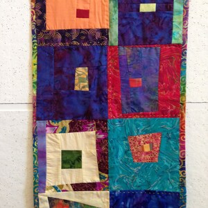Puede incluir: Una colcha de retazos colorida con una variedad de telas y patrones. La colcha est&aacute; hecha de cuadrados y rect&aacute;ngulos, y los colores incluyen morado, azul, verde, rojo, naranja y blanco.