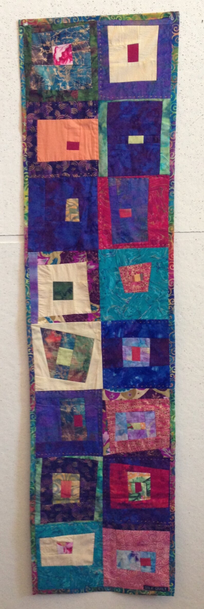Puede incluir: Una colcha de retazos colorida con una variedad de telas y patrones. La colcha est&aacute; hecha de cuadrados y rect&aacute;ngulos, y presenta una variedad de colores, incluyendo rojo, azul, verde y morado. La colcha est&aacute; bordeada con un ribete dorado. La colcha est&aacute; etiquetada como "Silk Quilt".