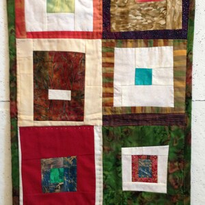 Puede incluir: Una colcha con un dise&ntilde;o de patchwork que presenta cuadrados de diferentes colores y patrones, incluyendo rojo, verde, marr&oacute;n y blanco. Los cuadrados est&aacute;n dispuestos en un patr&oacute;n de cuadr&iacute;cula, y la colcha est&aacute; bordeada con un borde blanco.
