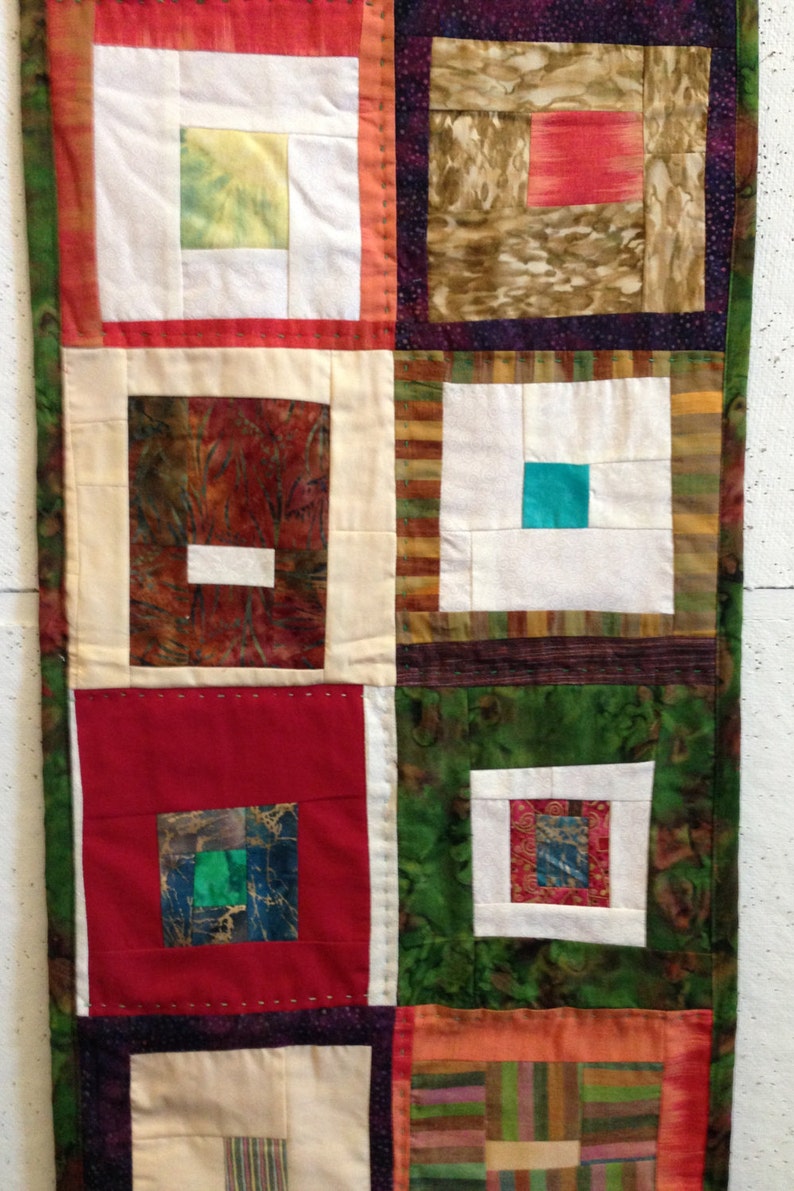 Puede incluir: Una colcha con un dise&ntilde;o de patchwork que presenta cuadrados de diferentes colores y patrones, incluyendo rojo, verde, marr&oacute;n y blanco. Los cuadrados est&aacute;n dispuestos en un patr&oacute;n de cuadr&iacute;cula, y la colcha est&aacute; bordeada con un borde blanco.