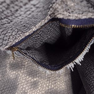 May include: Close-up of a gray and white patterned fabric with a zipper. The zipper is gold-colored and the fabric has a textured appearance. The interior of the fabric is visible.