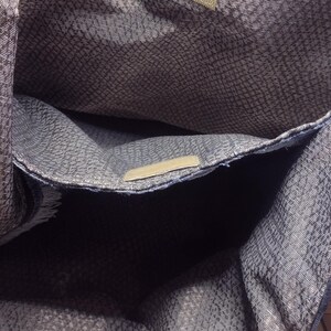 May include: A denim tote bag with a patterned interior. The bag has a rectangular shape with a large main compartment and a smaller pocket. The interior fabric has a gray and white pattern. The bag has a light blue denim exterior.