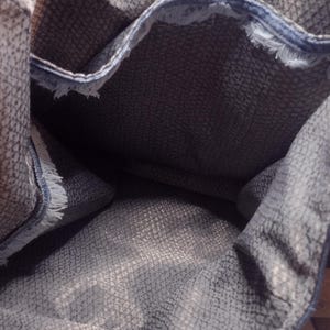 May include: A denim tote bag with a textured gray interior. The bag has frayed edges and denim handles. The interior fabric has a subtle pattern. The bag is open, showing the inside.