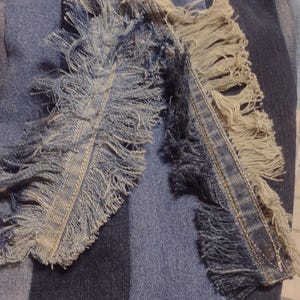 May include: Close-up of denim fabric with a patchwork design. Two fringed denim pieces are laid over the patchwork, showcasing frayed edges and a mix of light and dark blue hues. The overall texture is rough and casual.