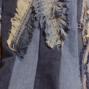 May include: Close-up of a denim textile with a patchwork design. The fabric features various shades of blue denim, with frayed edges and a striped pattern. The design includes a decorative fringe.