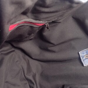 May include: Black tote bag interior with a red pocket and a zipper closure. The bag appears to be made of a soft, dark fabric. A small denim patch is visible on the side.