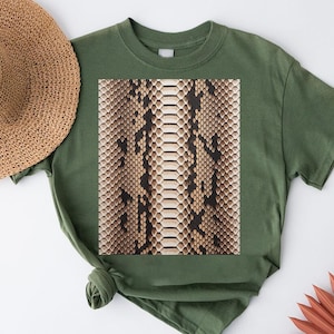 May include: An olive green t-shirt with a snakeskin print. The snakeskin design is in shades of brown, beige, and cream. A straw hat is visible in the upper left corner. The shirt is knotted at the bottom.