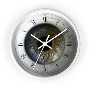 May include: White wall clock with a unique design. The clock face features a detailed image of a human eye, with blue and brown iris. Roman numerals mark the hours, and white hands indicate the time.