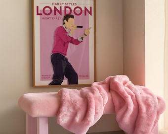 May include: A framed poster featuring a stylized illustration of Harry Styles performing, with the text HARRY STYLES LONDON NIGHT THREE WEMBLEY STADIUM 17.06.26. The poster is displayed above a pink bench covered with a soft, textured pink throw blanket.