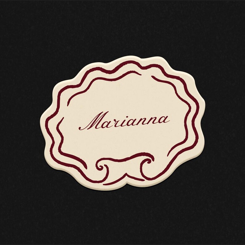Pode incluir: Cart&atilde;o de nome creme com borda ondulada e o nome "Marianna" em escrita bord&ocirc;. O cart&atilde;o tem enfeites decorativos bord&ocirc; na parte inferior. O fundo &eacute; preto.
