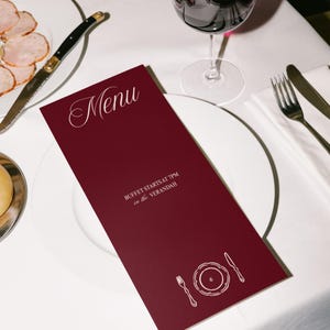 Pode incluir: Um cart&atilde;o de menu bord&ocirc; com a palavra "Menu" em escrita elegante. O cart&atilde;o inclui o texto "BUFFET STARTS AT 7PM in the Verandah" e um gr&aacute;fico de um prato, garfo e faca. Um copo de vinho e talheres tamb&eacute;m s&atilde;o vis&iacute;veis.