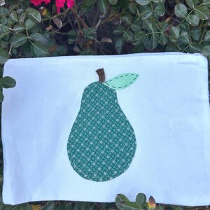 May include: A white zippered pouch with a green pear design. The pear is made of fabric with a small green and white pattern.