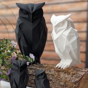 Könnte beinhalten: Geometrische Eulen-Skulpturen in Schwarz und Weiß. Die Eulen werden auf einem Baumstamm und einer weißen Oberfläche präsentiert. Die Skulpturen haben ein modernes, eckiges Design mit sichtbaren Facetten.