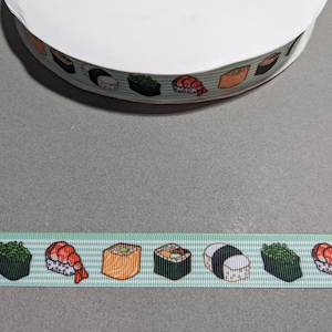 May include: A spool of light green grosgrain ribbon featuring a repeating pattern of various sushi rolls and shrimp nigiri. The ribbon has a textured, ribbed surface with a consistent horizontal orientation of the colorful food illustrations.