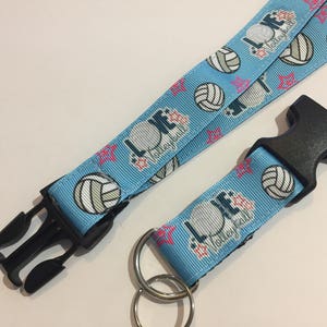 May include: Light blue volleyball lanyard with black plastic clasp and key ring. The lanyard features volleyballs, pink stars, and the words "LOVE Volleyball" in white and navy blue.