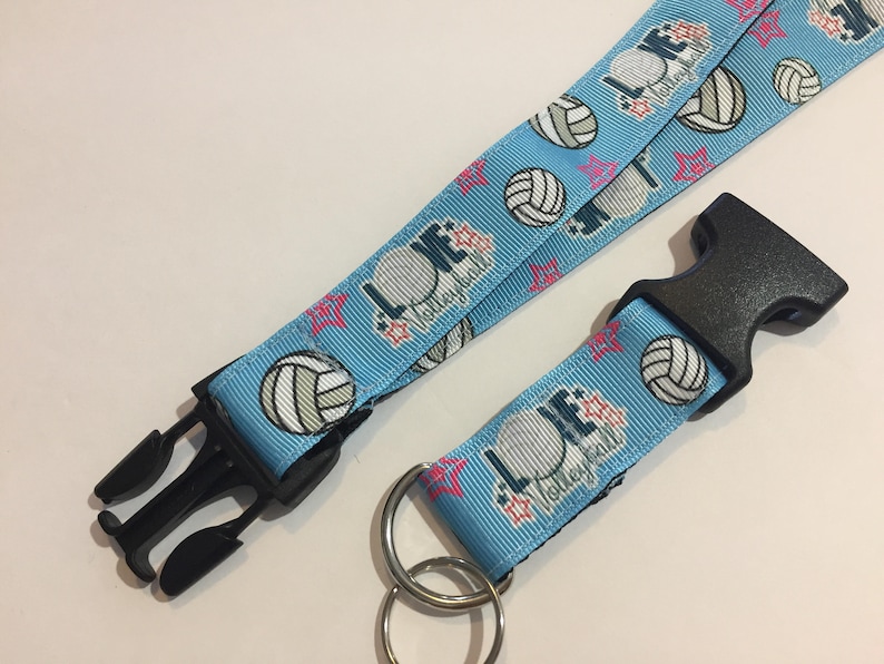 May include: Light blue volleyball lanyard with black plastic clasp and key ring. The lanyard features volleyballs, pink stars, and the words "LOVE Volleyball" in white and navy blue.