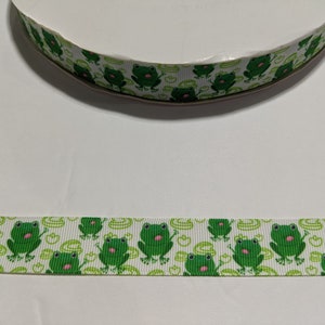 May include: White ribbon with a repeating pattern of green frogs with pink tongues on a white background.