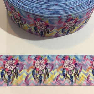 Pu&ograve; includere: Un rotolo di nastro blu con un motivo colorato di acchiappasogni. Il nastro presenta uno sfondo a chevron con accenti rosa, gialli e blu. Gli acchiappasogni sono circondati da piume e fiori.