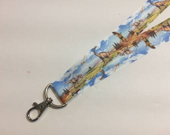 May include: A white lanyard with a colorful dinosaur print. The lanyard has a silver metal clip.