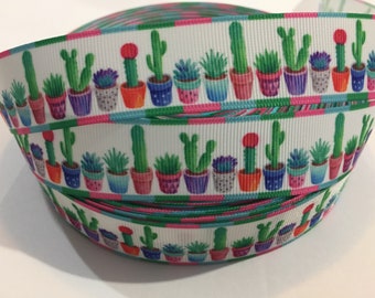 May include: A white ribbon with a repeating pattern of colorful potted cacti and succulents. The ribbon is folded and rolled up, showing multiple rows of the pattern.