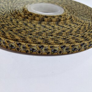 May include: A roll of patterned ribbon featuring a bee and honeycomb design on a yellow background. The ribbon is tightly wound, displaying the repeating pattern. Suitable for crafts, gift wrapping, or decorative applications. The ribbon is likely measured in meters.