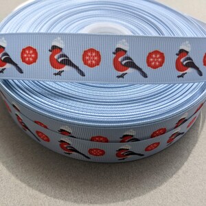 May include: A roll of light blue ribbon with a repeating pattern of red robins wearing white hats and red snowflakes.