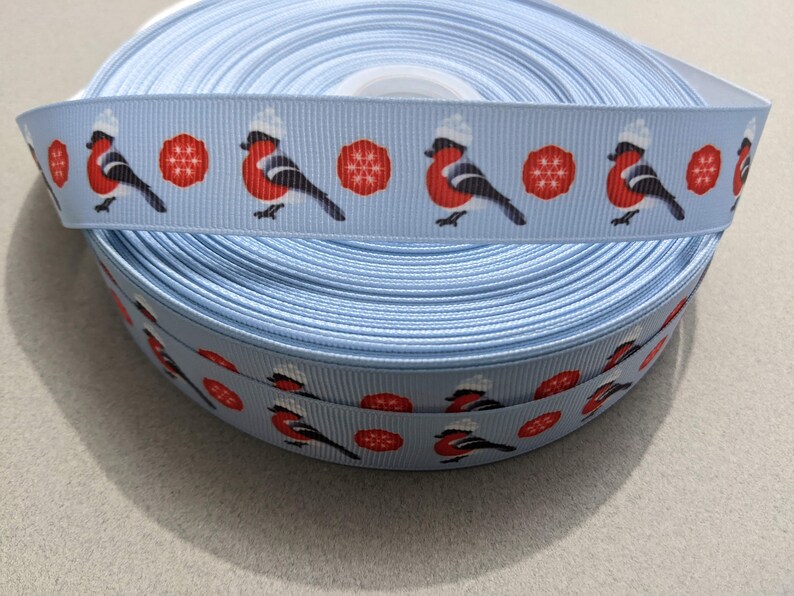 May include: A roll of light blue ribbon with a repeating pattern of red robins wearing white hats and red snowflakes.