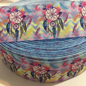 Pu&ograve; includere: Un rotolo di nastro blu con un motivo a chevron bianco e rosa e un motivo ripetuto di acchiappasogni con piume e fiori.