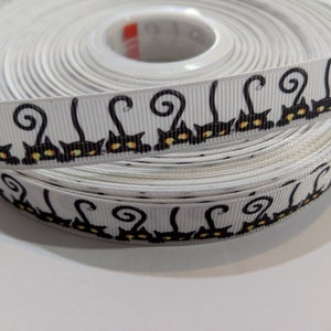 May include: A roll of white ribbon with a black and orange repeating pattern of cats with curled tails.