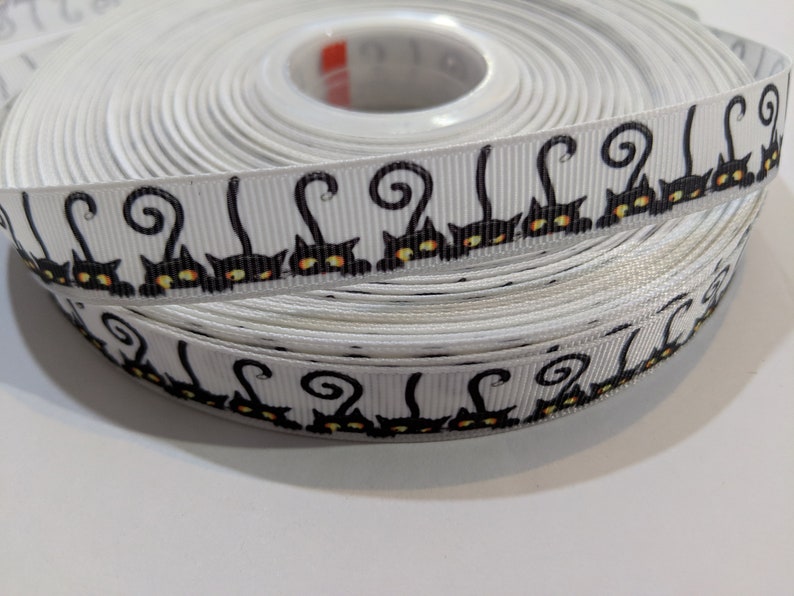 May include: A roll of white ribbon with a black and orange repeating pattern of cats with curled tails.