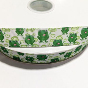May include: A roll of white ribbon with a green frog pattern. The ribbon is on a white spool.