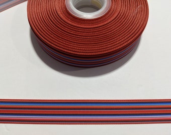 May include: Red, blue, and white striped ribbon with a subtle ombre effect. The ribbon is wound around a spool.