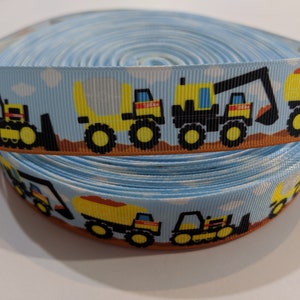 May include: A roll of blue ribbon with a repeating pattern of yellow construction vehicles on a brown background. The vehicles include a dump truck, an excavator, and a bulldozer.