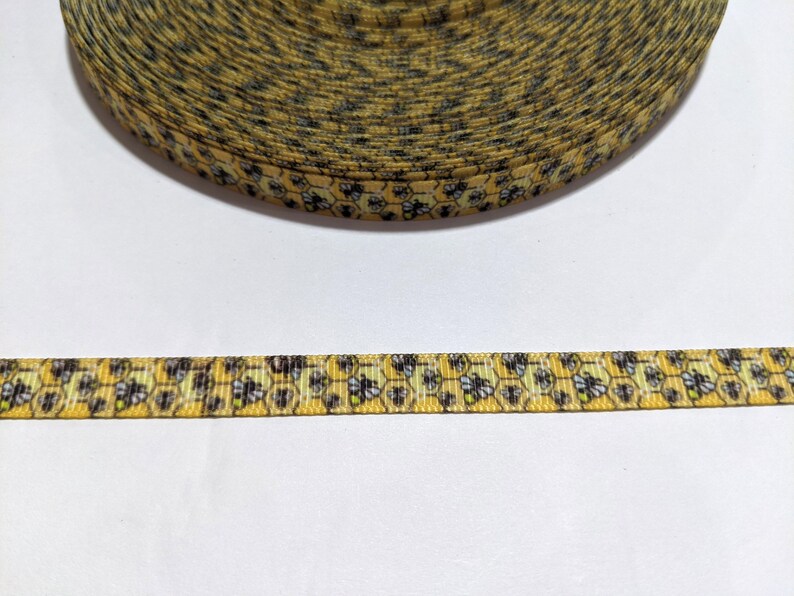 May include: A roll of yellow ribbon featuring a repeating pattern of bees and honeycomb. The ribbon is approximately 1.3 cm wide, ideal for crafts, gift wrapping, or other decorative purposes.