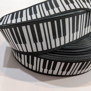 May include: Black and white piano key patterned ribbon. The ribbon is rolled up and the pattern is visible on both sides.