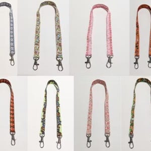 May include: Collection of eight patterned bag straps in various colors. Designs include floral, geometric, and animal prints. Each strap has silver-tone metal swivel clasps for easy attachment to a bag. The straps are displayed against a white background.