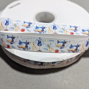 Peut inclure: Un ruban blanc avec un motif répété de machines à coudre bleues, de pommes rouges, de ciseaux et de bobines de fil.