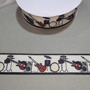 Puede incluir: Una cinta blanca con borde negro y un patrón repetido de guitarras eléctricas, baterías y platillos negros y blancos.