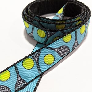 May include: A blue and black ribbon with a repeating pattern of tennis rackets and tennis balls.