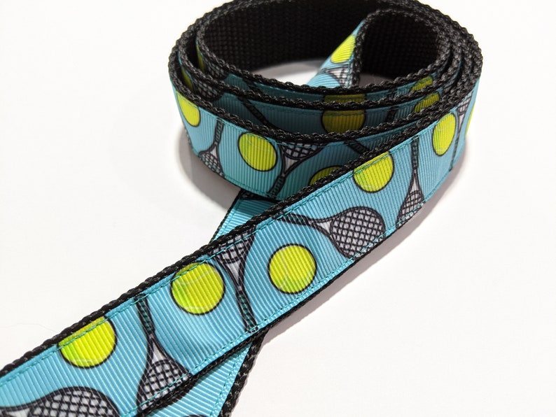 May include: A blue and black ribbon with a repeating pattern of tennis rackets and tennis balls.