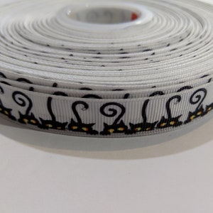 May include: White ribbon with a black cat design. The cats have curled tails and yellow eyes.