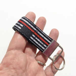 May include: Black and white striped key chain with a red stripe and a silver key ring. The keychain has a distressed American flag design.