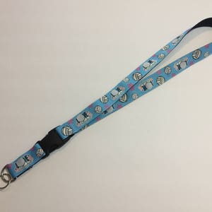 May include: A light blue lanyard with a black buckle and a silver key ring. The lanyard features a pattern of volleyballs, stars, and the text "LOVE Volleyball". The lanyard is approximately 36 inches long.