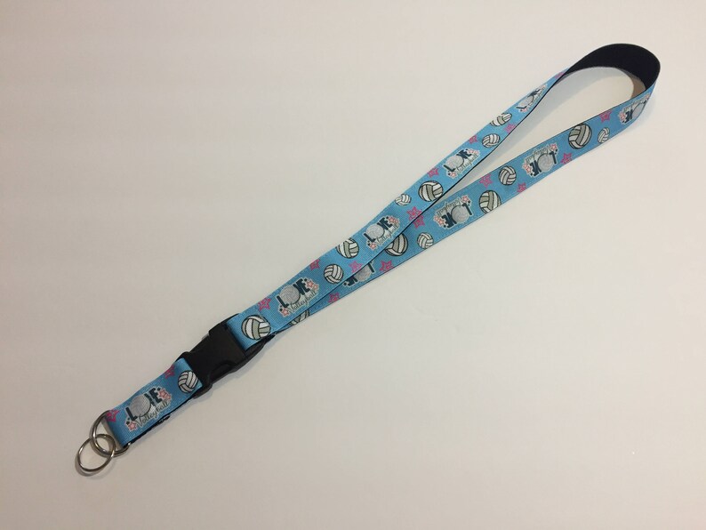 May include: A light blue lanyard with a black buckle and a silver key ring. The lanyard features a pattern of volleyballs, stars, and the text "LOVE Volleyball". The lanyard is approximately 36 inches long.